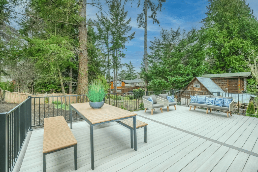 Spacious outdoor deck with modern patio furniture and table, surrounded by tall trees and greenery.