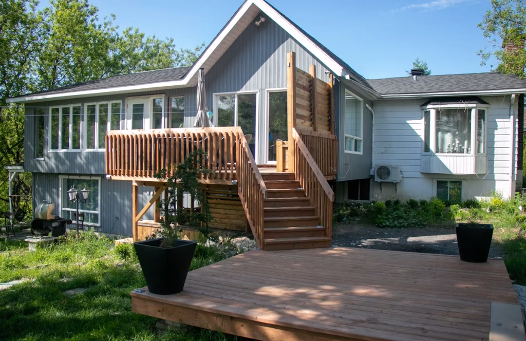 Freshly stained wooden deck with stairs attached to a gray house on a sunny day.