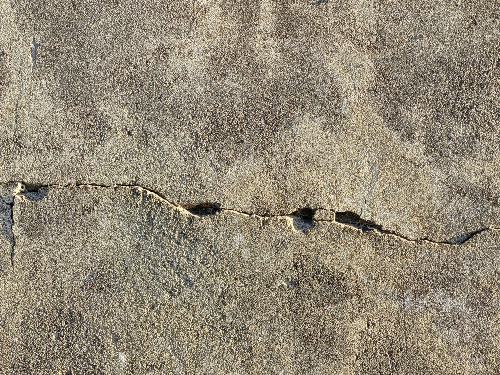 Close-up view of a cracked and weathered concrete surface, showing damage and structural wear.
