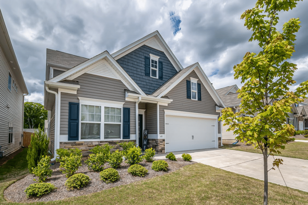 Two-story suburban home with gray and blue siding, white trim, attached garage, landscaped front yard, and clean gutters visible along the roofline under a cloudy sky.